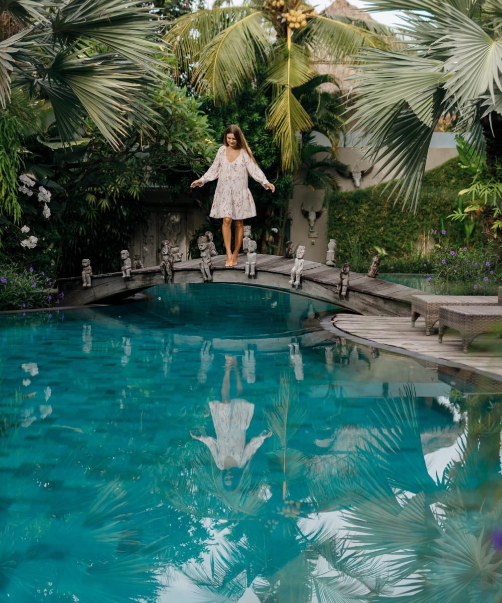Beautiful young brunette wearing stylish dress laughing while walking  on poolside located in yard of villa on summer sunny day